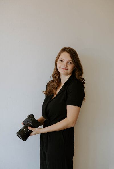 kylie posing for her branding portraits while holding her camera, looking at the camera 