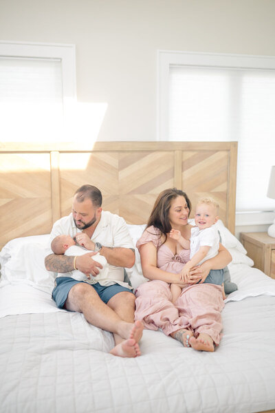 A pregnant mother stands on the beach with her young child, both smiling and enjoying the moment. The golden light reflects off the water, creating a peaceful scene. Captured by a Westport photographer, this beautiful maternity moment is set against the serene beach backdrop