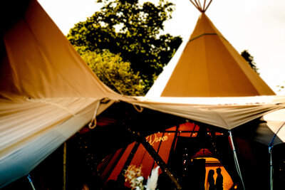 an artistic photograph of a silhouetted couple in the light showing their tipi in full view