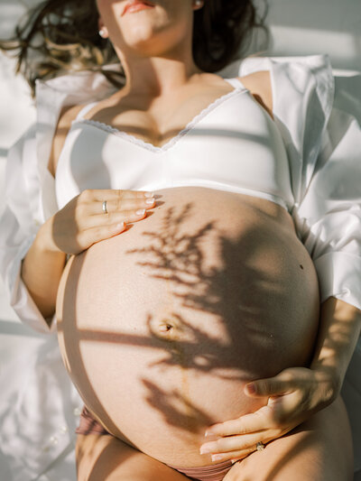 Maternity photography in Pearland Texas. Mom holding belly with flower shadow cast across her- captured by AMP.