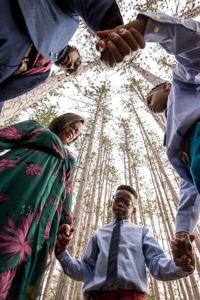 a Black family holds hands while the photographer lays on the ground, shooting upwards