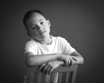 childrens portrait in studio of boy sitting backwards on chair with heavy shadow