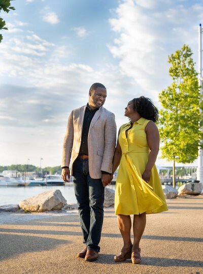 An African-American couple hold hands and walk by water..