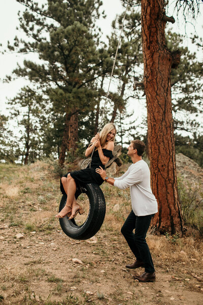 Engaged couple play on tire swing