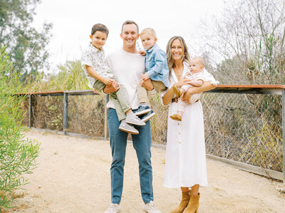 Mom and dad holding three young boys standing on a outdoor trail during a home family photo session.
