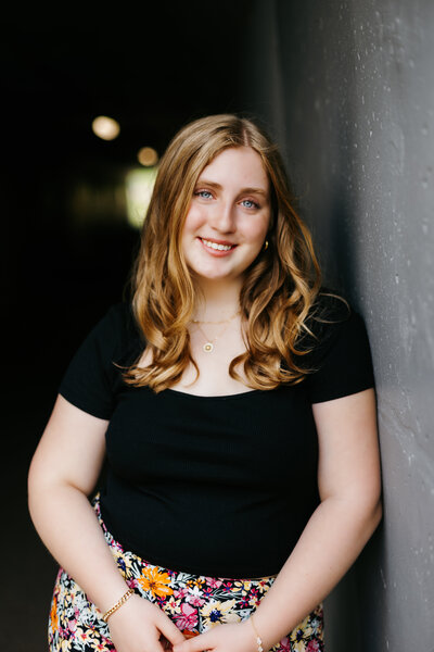 Senior girl in a black top leaning against a gray wall
