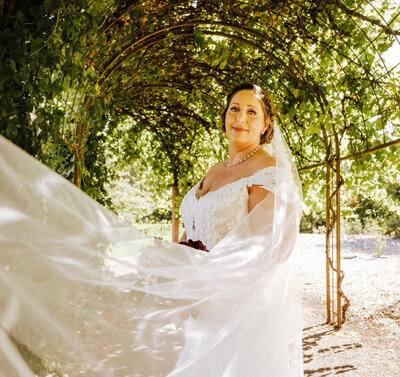 bride standing under and arbor with her custom bridal veil with pearls