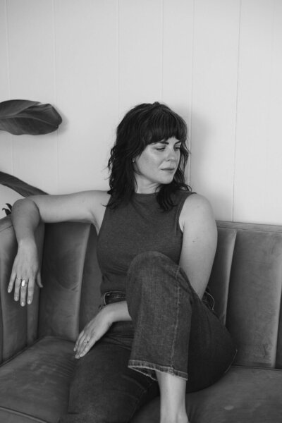 Web designer Carrie of Bloem Creations sits on a couch and looks off to the side.