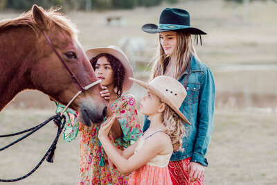 3 children petting the nose of a brown horse