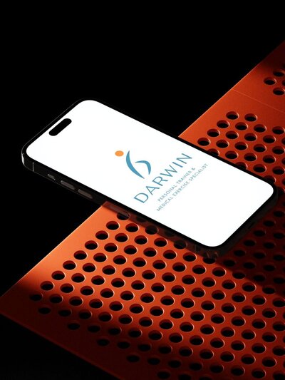 Smartphone displaying Darwin’s brand mark and text in copper and recovery blue, set against a dynamic, modern orange perforated metal surface—emphasizing tech-forward brand versatility.