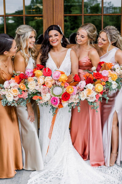 Bride with bridesmaids holding bright bouquets of pinks, reds and oranges