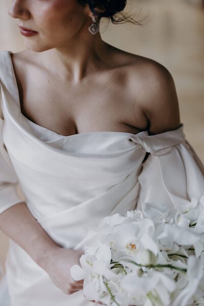 A close-up of a bride's off-the-shoulder dress and luxurious white flower bouquet