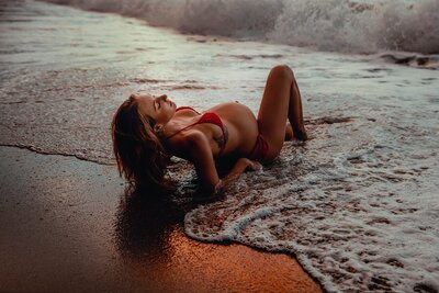 Pregnant woman laying on black sand beach in Maui Hawaii