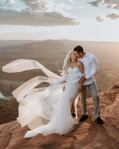 bride and groom kissing with the wind blowing her dress at dead horse state park