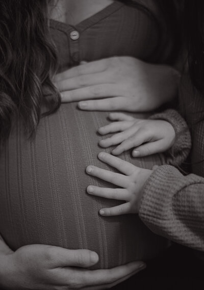 lose-up of a young child’s hands gently resting on their pregnant mom’s belly, capturing a sweet, intimate moment between siblings