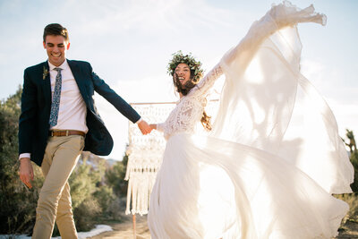having just eloped, a couple sitting on joshua tree boulders snuggle in close and smile.