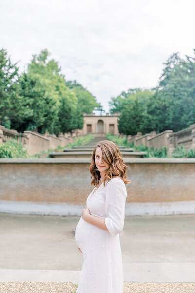 Pregnant woman standing with hands beneath belly in Meridian Hill Park, Washington DC maternity session