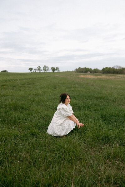 woman sitting alone in an open Kansas field wearing a white dress on a calm overcast day

