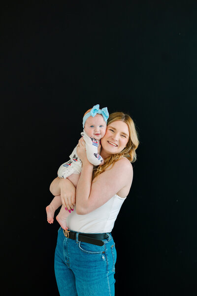 Aly Matei holding her baby in front of a black background