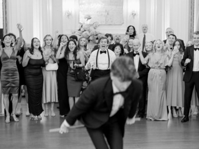 Flash photo of groom carrying bride through the line of their wedding guests while silver streamers fly around them