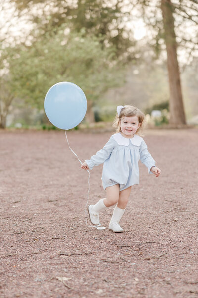 Portrait of a toddler running with a blue balloon.