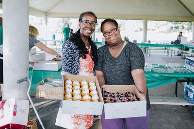 Two women hold boxes of cupcakes