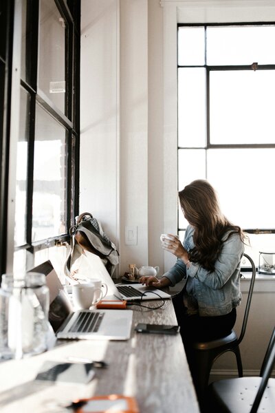 Productieve werksessie: Een vrouw is bezig met het samenstellen van een online programma terwijl ze een kop thee in haar hand houdt. Ervaar de combinatie van efficiëntie en ontspanning