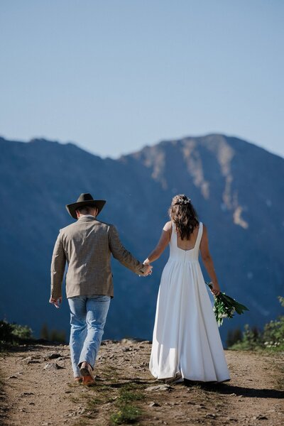 Wedding and Elopement Photography, bride and groom hold hands in front of Rocky Mountains during Colorado wedding day.