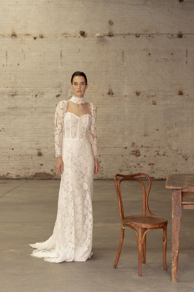 Bride wearing lace dress with collar standing by a chair