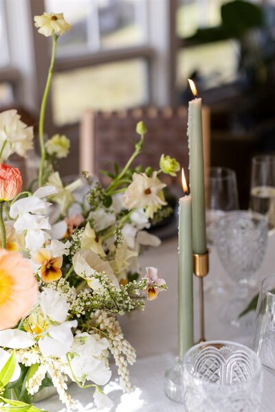 A thoughtfully designed tablescape with green taper candles, whimsical flower arrangements, and crystal glasses.