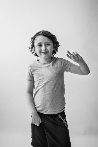 Black and white photograph of boy doing a peace sign and looking at the camera.