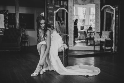 Black and white photo of bride fastening heeled shoe 