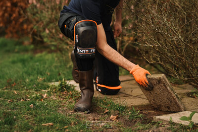 man haalt tegels uit de tuin met fento kniebeschermers aan en oranje handschoenen