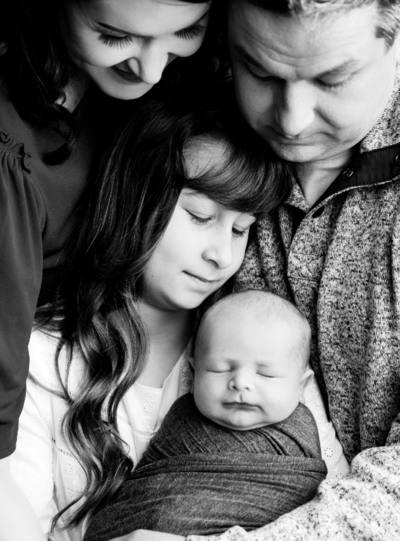 Family of four posing for photoshoot holding newborn baby