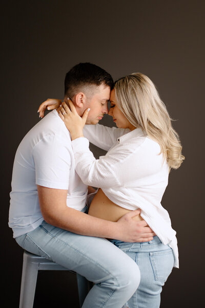 intimate studio style maternity portrait of husband and wife on white shirt and light denim jeans