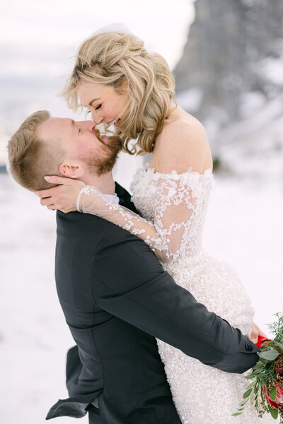 Groom lifting his bride on top of a snowy mountain.
