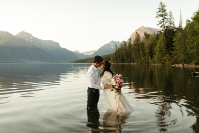 happily newly married couple kissing while standing in shallow lake, destination wedding photographer, elopement wedding