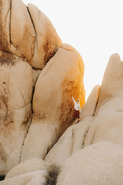 woman standing on large rock formations holding her arm in the air