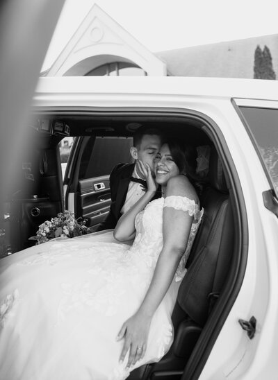 groom kissing bride on the cheek while they are sitting in a limo