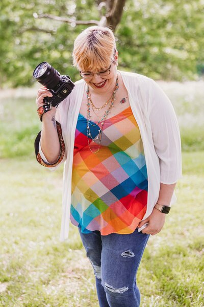 St Louis MO photographer walking with her camera in her hand and a colorful top smiling