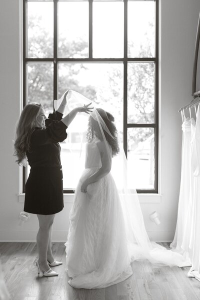 Bride trying on a wedding dress as a stylist adjusts her veil.