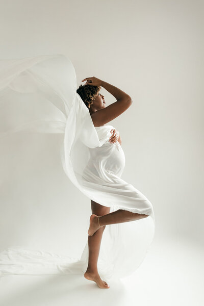 woman moves with white flowing fabric and pregnant belly for maternity photos