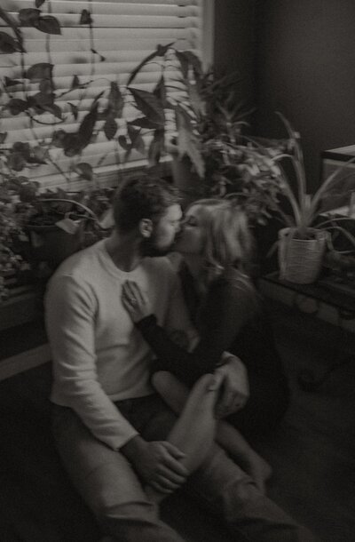 In-home session of a couple in their home. They're hanging out on the floor in their sunroom surrounded by a bunch of plants.