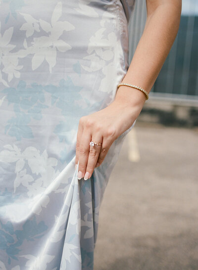 Fine art close-up of bride’s hand gathering floral-embossed silk gown with natural light and soft editorial composition.