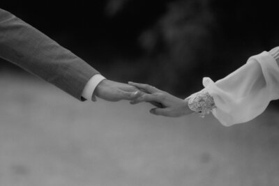 Ein schwarz-weiß Bild von zwei übereinanderliegenden Händen eines Hochzeitspaares, die leicht ineinander verschränkt sind.