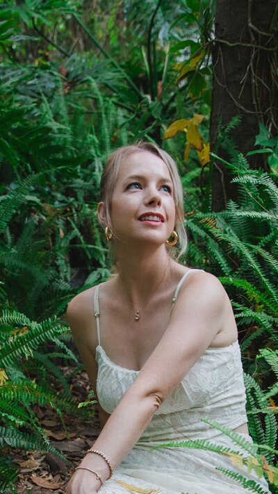 Woman sitting in forest looking up at the sky smiling
