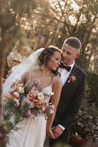 Romantic golden hour outdoor wedding bridal party moment with sunlight filtering through trees and a beautiful soft pink floral bouquet at Blockhouse venue near downtown Portland, Oregon.