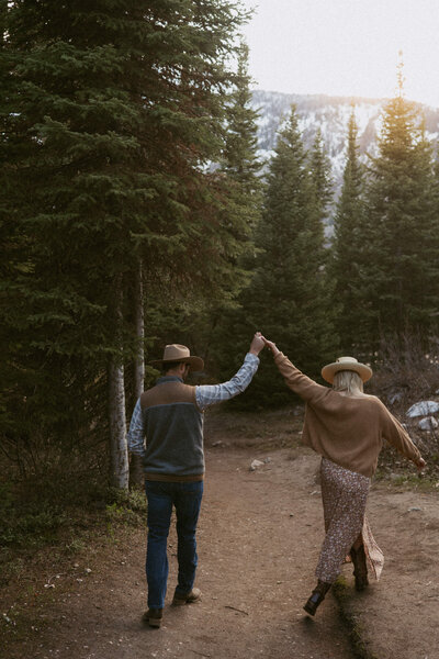 a couple walking along a forest path in Grand Teton national park as the sun sets behind the trees