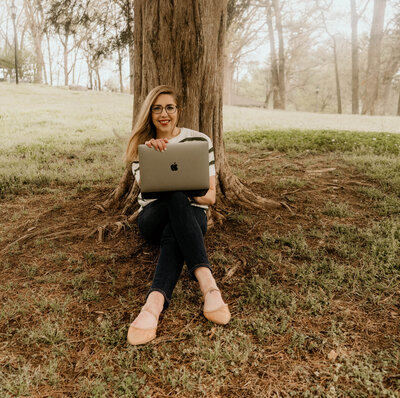 Heather Sackett sitting in front of tree with legs crossed and open computer on lap