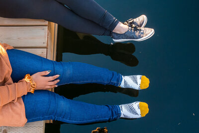 Two people sitting on the end of a dock with their feet dangling over the water.